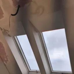 Poddasze z oknami dachowymi w trakcie prac wykończeniowych. Widoczne ślady szpachlowania na ścianach i suficie, wystające przewody elektryczne.