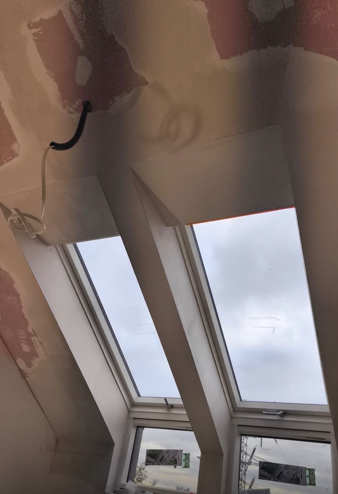 Poddasze z oknami dachowymi w trakcie prac wykończeniowych. Widoczne ślady szpachlowania na ścianach i suficie, wystające przewody elektryczne.