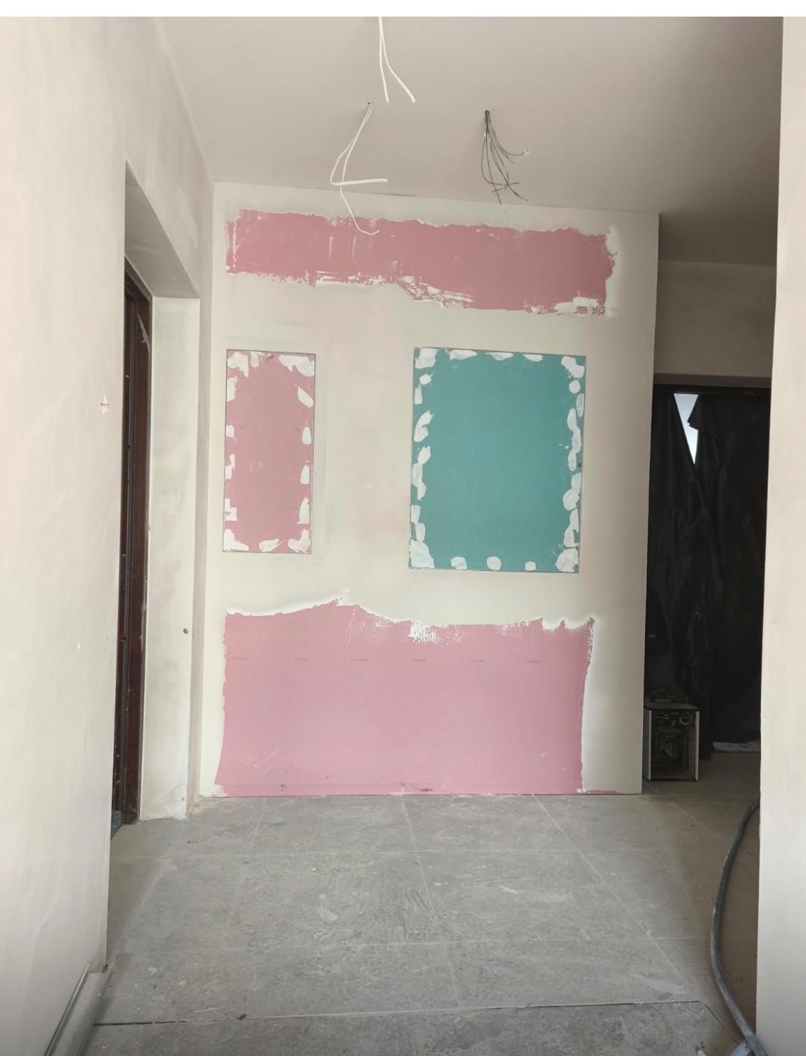 Ściana po szpachlowaniu z fragmentami pomalowanymi na różowo i niebiesko, widoczne kable zwisające z sufitu, przygotowanie do malowania w trakcie remontu.