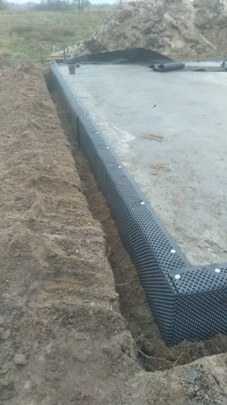 Fundamenty z izolacją pionową w wykopie. Widoczna folia kubełkowa przymocowana do betonu, zabezpieczenie przed wilgocią gruntową.
