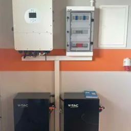 Kompletna instalacja fotowoltaiczna z dwoma akumulatorami V-TAC, inwerterem Deye oraz rozdzielnicą elektryczną, zamontowana na ścianie z pomarańczowym pasem.