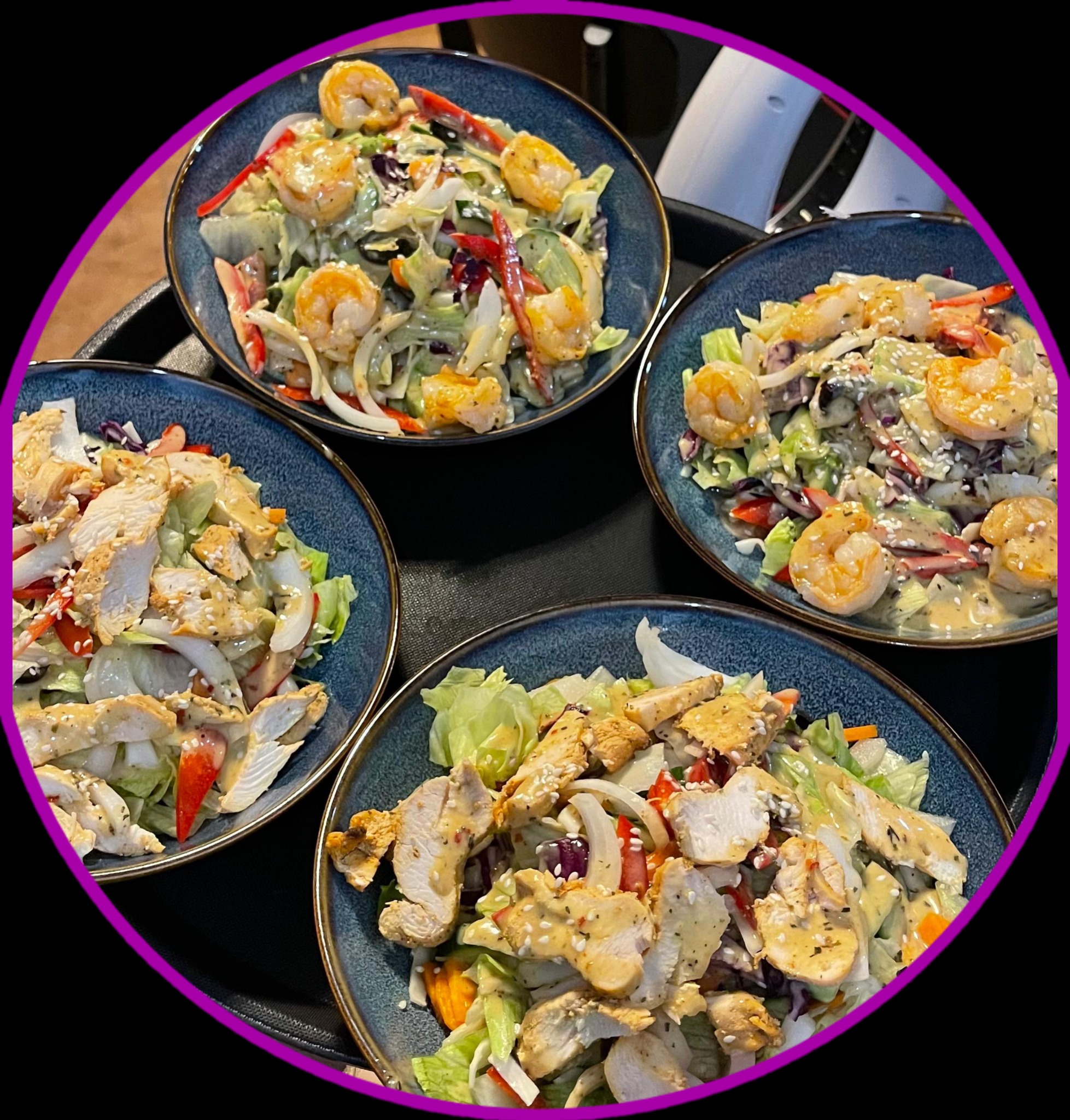 Cztery miski sałatek: dwie z krewetkami, dwie z kurczakiem, podane na czarnej tacy z fioletową obwódką. Dania gotowe do serwowania, z bliska, ostre.