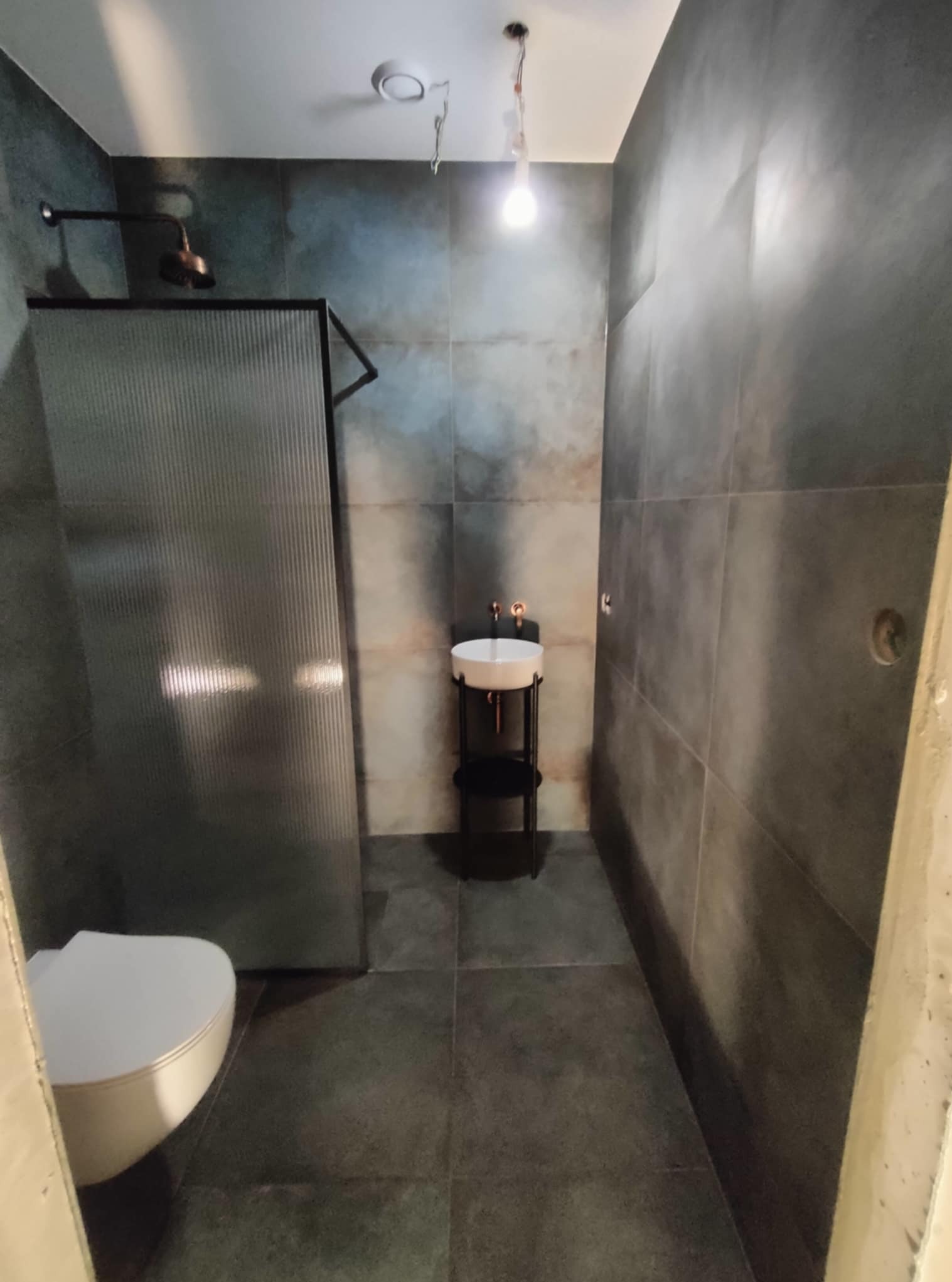 Nowoczesna łazienka w odcieniach szarości z kabiną prysznicową ze szkła ryflowanego i umywalką na metalowym stelażu. Minimalistyczny design, surowe wykończenie ścian.