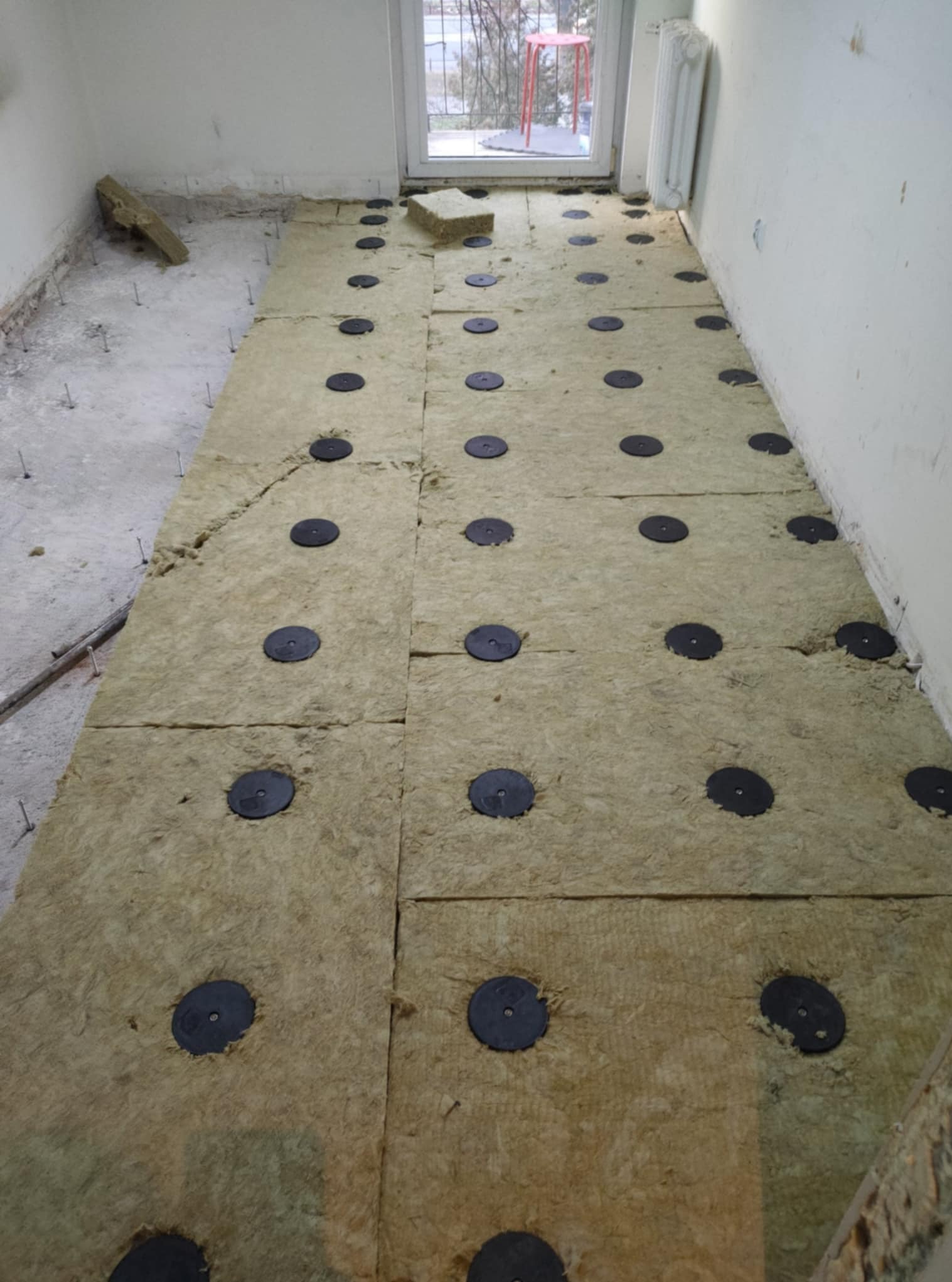 Izolacja podłogowa z wełny mineralnej i czarnych podkładek w trakcie prac w Warszawie. Widoczne przygotowania do dalszych etapów wykończenia.
