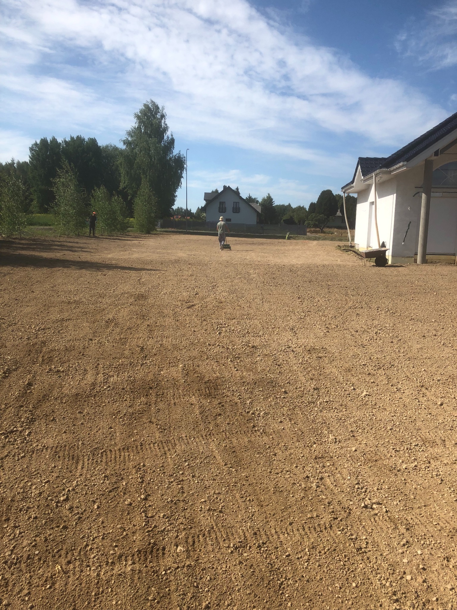 Przygotowany teren pod przyszły ogród w Lublinie. Dwóch mężczyzn podczas niwelacji terenu. W tle drzewa i budynki.