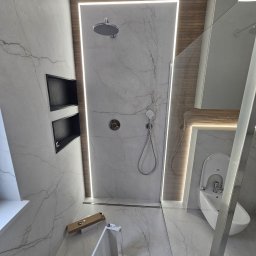 Wardega-budd - Nowoczesna łazienka z marmurowymi płytkami, podświetlanym prysznicem typu walk-in i bidetem. Widoczna armatura w kolorze chromu i elementy montażowe.
