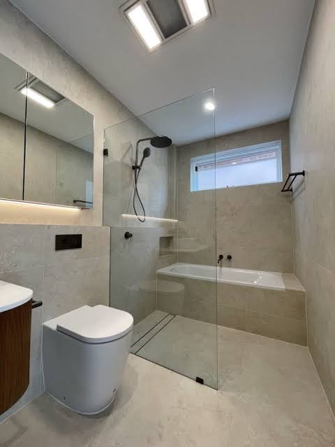 Nowoczesna łazienka z kabiną prysznicową typu walk-in, umywalką z drewnianą szafką, podwieszaną toaletą i dużym lustrem. Stonowana kolorystyka, minimalistyczny design.