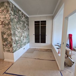 D PAUL LTD - Pokój w trakcie wykańczania: wzorzysta tapeta z motywem roślinnym, zabudowana szafa z ciemnymi szybami, zabezpieczona podłoga. Widoczne kartony i narzędzia.