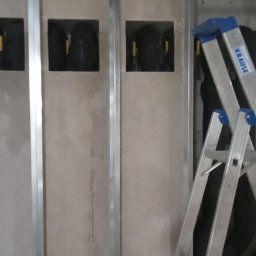 BUD-PROFEKT MYKOLA FEDKOVYCH - Montaż płyty karton gips na metalowym stelażu z widocznymi otworami na instalacje. W tle drabina Krause. Prace wykończeniowe w trakcie realizacji.