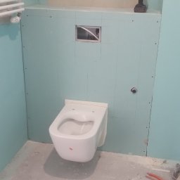 Montaż podwieszanej toalety na ścianie z płyt kartonowo-gipsowych w łazience. Widoczne narzędzia i instalacja. Etap prac wykończeniowych.