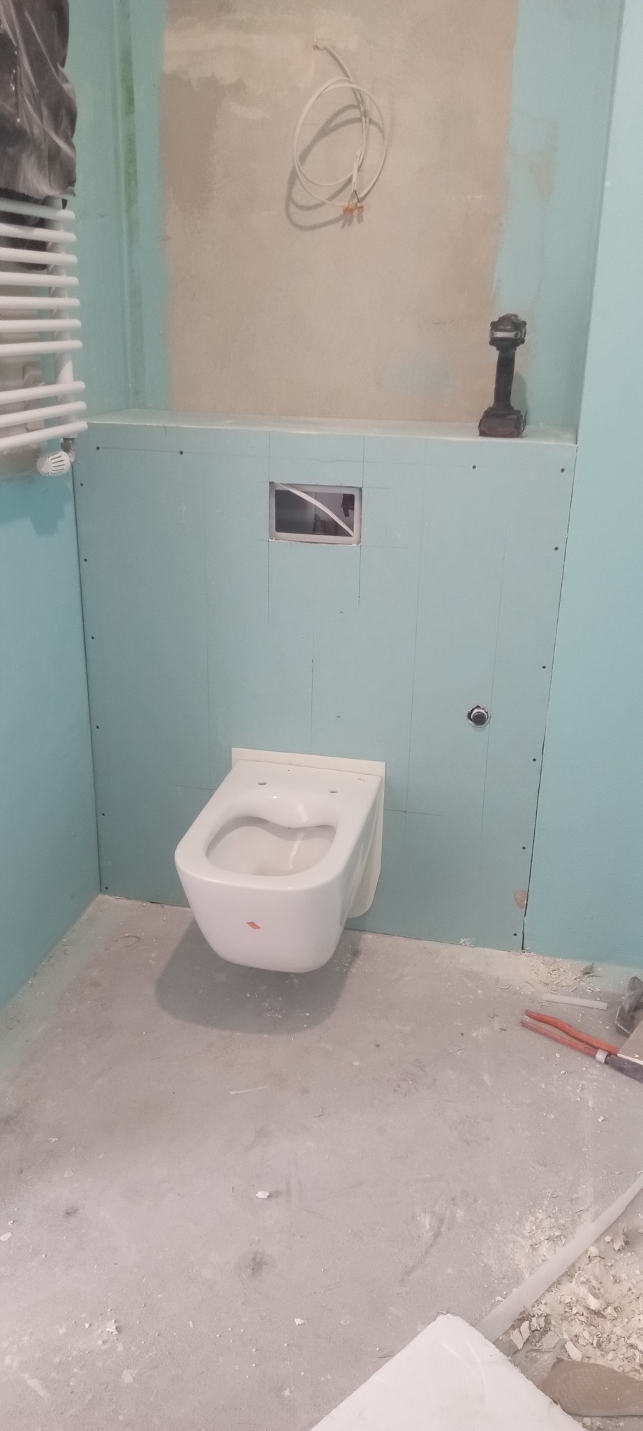 Montaż podwieszanej toalety na ścianie z płyt kartonowo-gipsowych w łazience. Widoczne narzędzia i instalacja. Etap prac wykończeniowych.