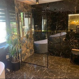 KORTIN - Ekskluzywna łazienka w ciemnym marmurze ze złotymi żyłami, kabina prysznicowa typu walk-in, wolnostojąca wanna i dekoracyjna mozaika heksagonalna.