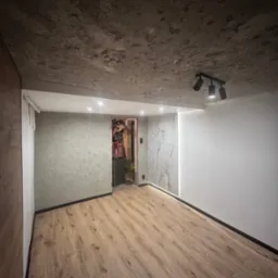 Wykończone wnętrze: panele podłogowe, ściany z efektem betonu i marmuru, oświetlenie punktowe. Widok na otwarte przejście do innego pomieszczenia.