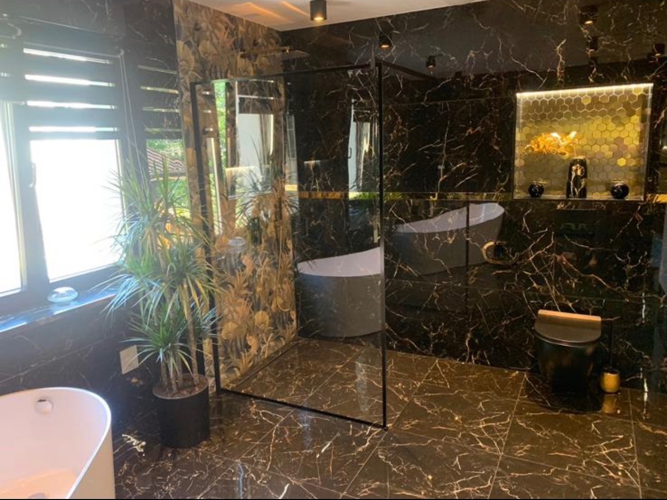 Ekskluzywna łazienka w ciemnym marmurze ze złotymi żyłami, kabina prysznicowa typu walk-in, wolnostojąca wanna i dekoracyjna mozaika heksagonalna.