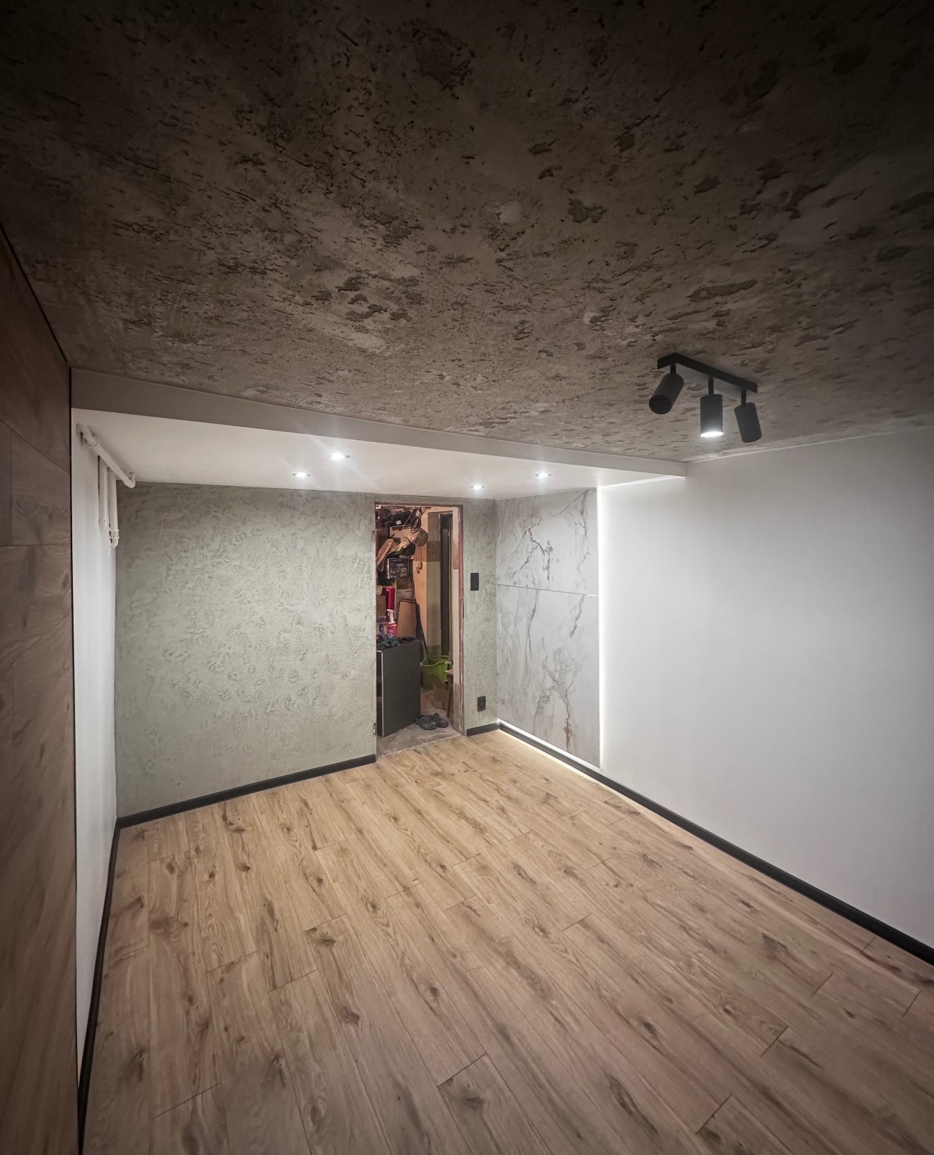 Wykończone wnętrze: panele podłogowe, ściany z efektem betonu i marmuru, oświetlenie punktowe. Widok na otwarte przejście do innego pomieszczenia.