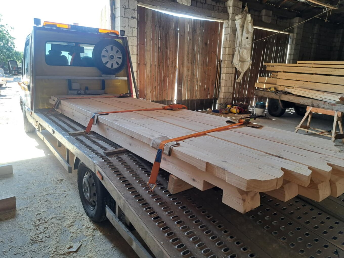 Laweta z drewnianymi elementami konstrukcyjnymi zabezpieczonymi pasami transportowymi. Widoczny warsztat w tle.