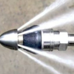 PERFECT CLEAN DANIEL MICHOŃ - Dysza udrażniająca rury pod ciśnieniem, woda tryska z otworów, metalowa konstrukcja, szary beton w tle. Widok z bliska.