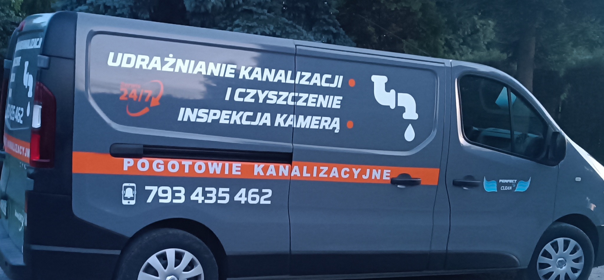 Szary samochód dostawczy z napisem „Udrażnianie kanalizacji” i numerem telefonu, zaparkowany na zewnątrz. Widoczne logo firmy „Perfect Clean”.