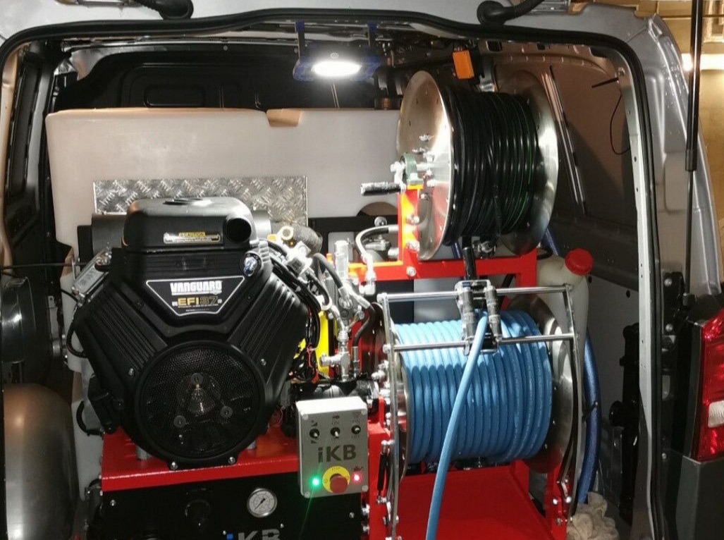 Wnętrze furgonetki z profesjonalnym sprzętem do czyszczenia: silnik Vanguard, zwijadła z wężami (czarny i niebieski), zbiornik na wodę i panel sterowania iKB.