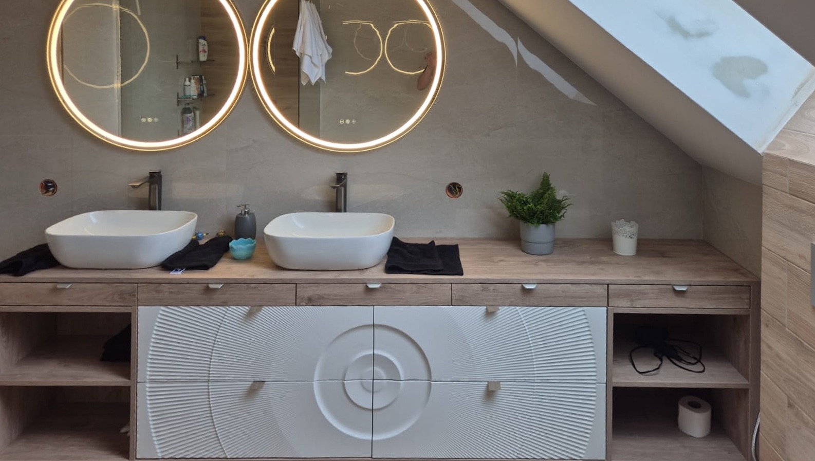 Nowoczesna łazienka na poddaszu z dwoma umywalkami nablatowymi, okrągłymi lustrami z podświetleniem LED i szafką z unikalnym wzorem na frontach.