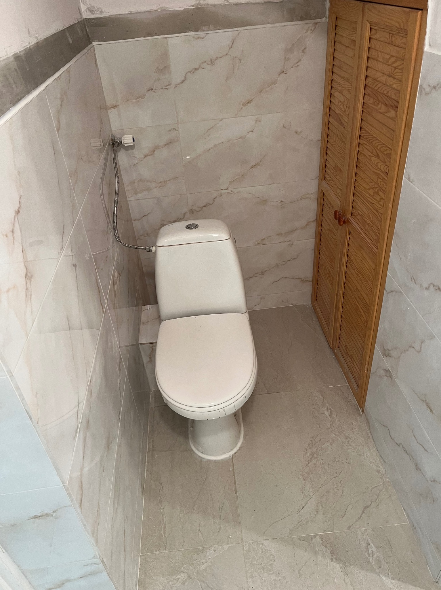 Wykończona toaleta z marmurowymi płytkami na ścianach i podłodze, drewniana szafka w rogu. Widok z góry na białą muszlę klozetową.