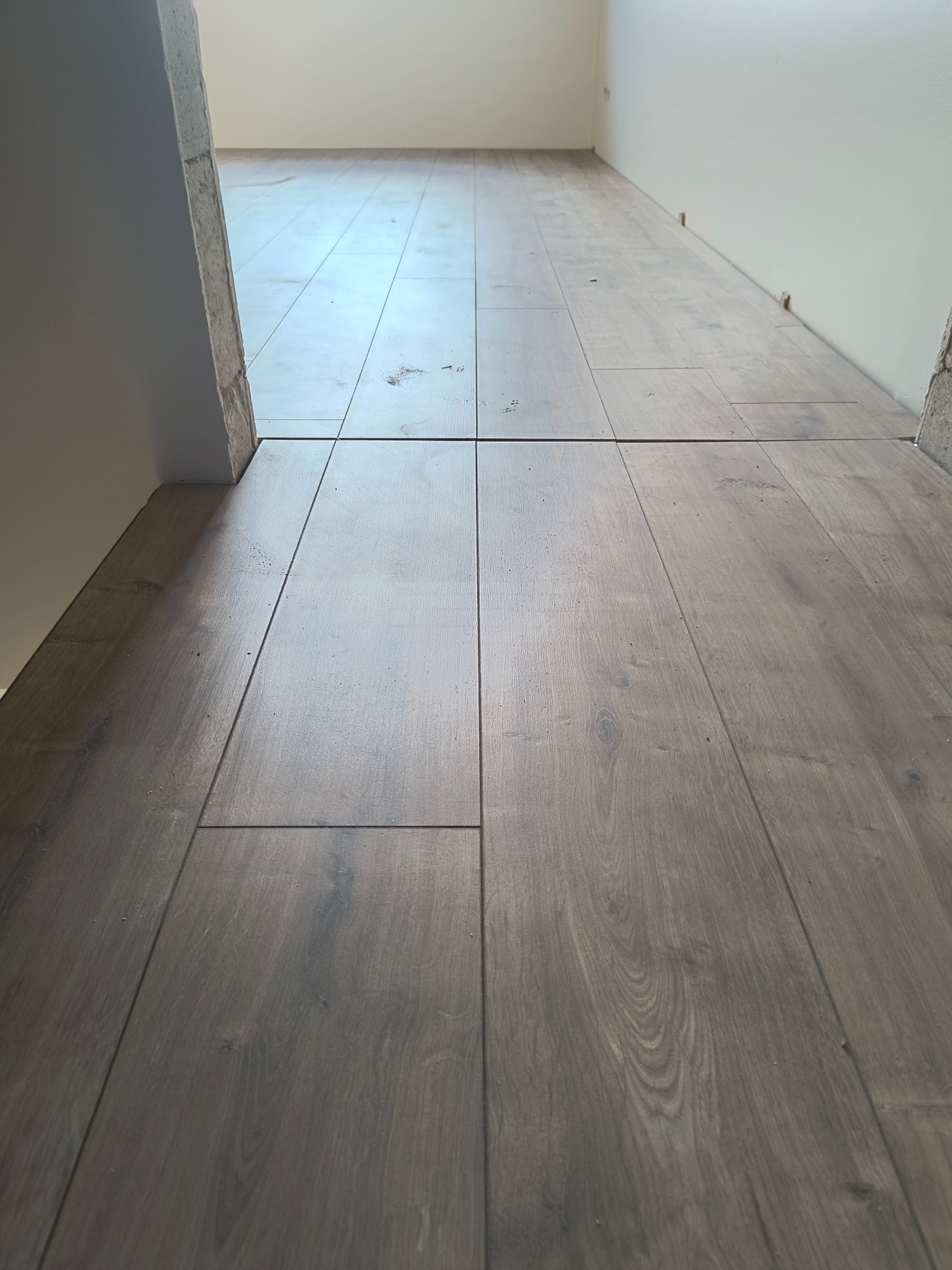 Ułożone panele podłogowe w korytarzu, widoczne z perspektywy podłogi. Brązowe panele z wyraźną fakturą drewna, jasne ściany w tle. Widok na dalszą część korytarza.