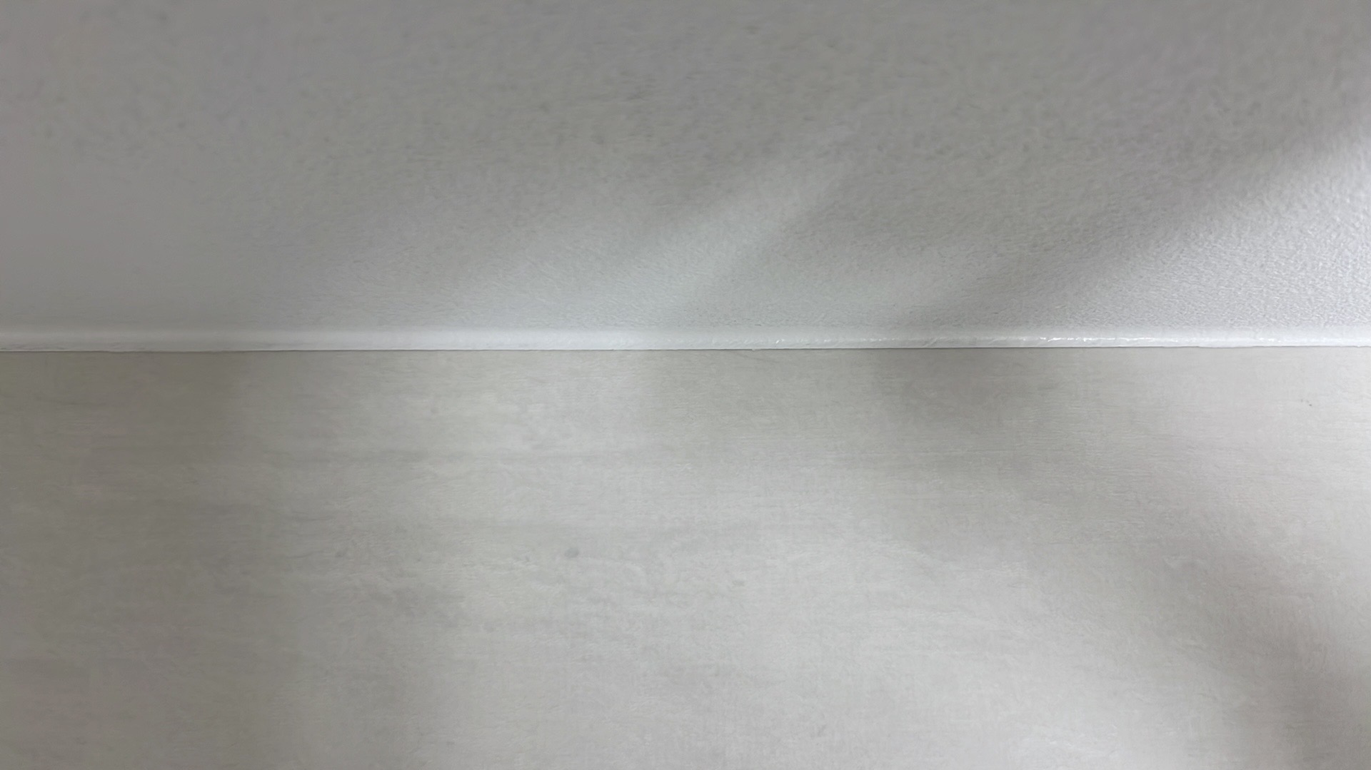 Gładka, szara ściana po szpachlowaniu i malowaniu, widok z dołu, z delikatnym cieniem na suficie. Minimalistyczne wykończenie wnętrza.