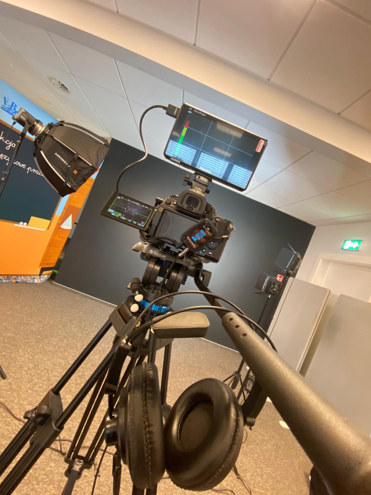 Kamera na statywie z podglądem obrazu, mikrofonem i słuchawkami w studiu. Oświetlenie studyjne w tle. Sprzęt do nagrywania filmów w pomieszczeniu.