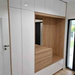 Krystian Zaręba - Nowoczesna szafa wnękowa z białymi frontami i drewnianymi akcentami, wbudowana w przedpokoju, z lustrem i szufladami. Minimalistyczny design, jasne wnętrze.