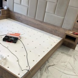 Krystian Zaręba - Montaż drewnianego łóżka z tapicerowanym zagłówkiem w odcieniach beżu. Widoczne narzędzia i elementy konstrukcyjne. Praca w toku.