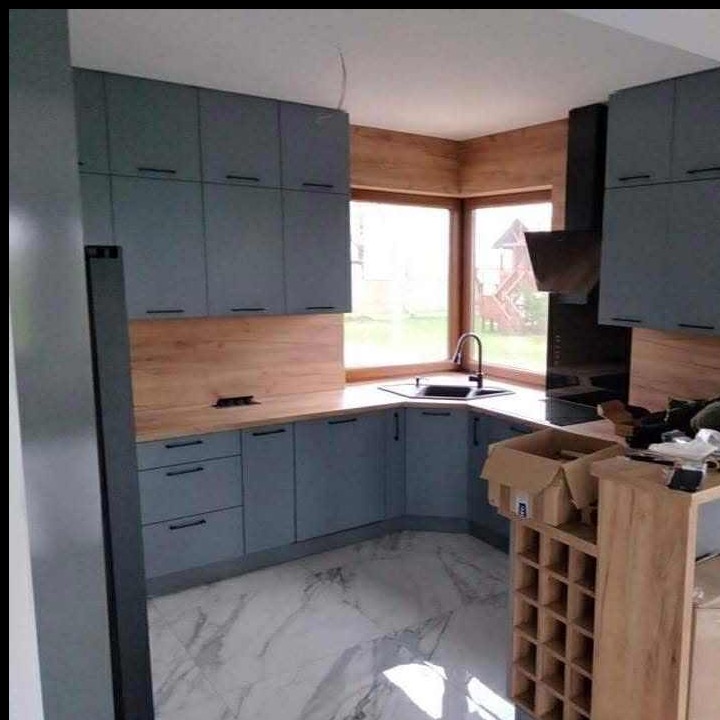 Szara kuchnia narożna z drewnianym blatem i oknem z widokiem na plac zabaw. Na podłodze marmurowe płytki. Częściowo widoczny regał na wino.