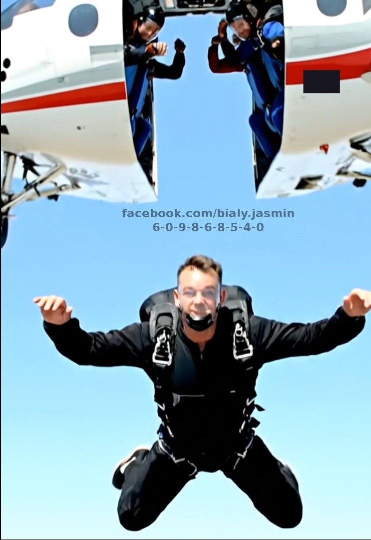 Skydiver w czarnym kombinezonie, skaczący z samolotu na tle błękitnego nieba. Widoczni inni skoczkowie w drzwiach samolotu. Na zdjęciu widnieją napisy.