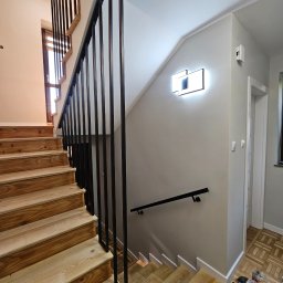 JS Welding & Renovation Jakub Siemieniec - Drewniane schody z czarną, metalową balustradą o minimalistycznym designie. Widoczne narzędzia na podłodze sugerują trwający montaż lub prace wykończeniowe.