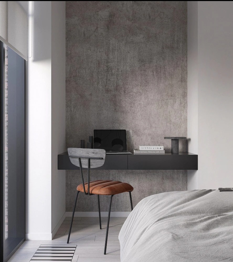 Nowoczesny pokój z biurkiem zawieszonym na ścianie i krzesłem z brązowym siedziskiem. Na biurku laptop, książki i dekoracje. Ściana w odcieniach szarości.
