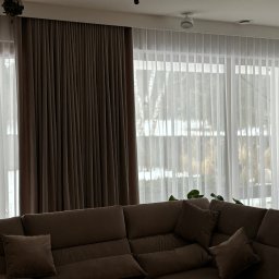 LaurAles Michał Marciniak - Eleganckie, brązowe zasłony i delikatne, białe firany w przestronnym salonie z dużym narożnikiem, tworzące przytulną atmosferę wnętrza.