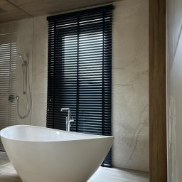 LaurAles Michał Marciniak - Elegancka łazienka z wolnostojącą wanną i czarnymi żaluzjami drewnianymi w oknie, zapewniającymi prywatność i kontrolę światła.