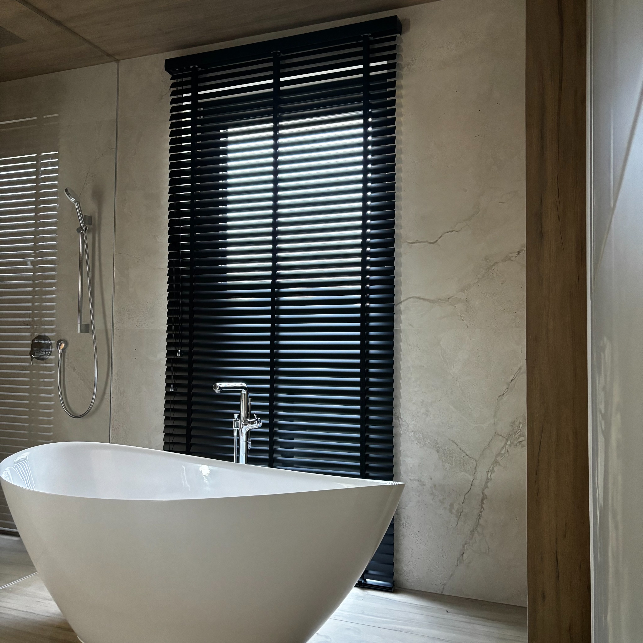 Elegancka łazienka z wolnostojącą wanną i czarnymi żaluzjami drewnianymi w oknie, zapewniającymi prywatność i kontrolę światła.