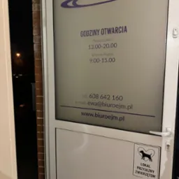 Wejście do biura rachunkowego E.J.M. z godzinami otwarcia na szybie i naklejką 'Lokal przyjazny zwierzętom' na drzwiach. Widoczne dane kontaktowe i logo firmy.