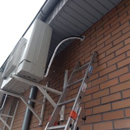 KLIMANTEK Andrzej Tuczyński - Instalacja klimatyzacji na ceglanej ścianie budynku. Widoczne jednostki zewnętrzne i drabina Krause. Ujęcie z dołu, podkreślające montaż.