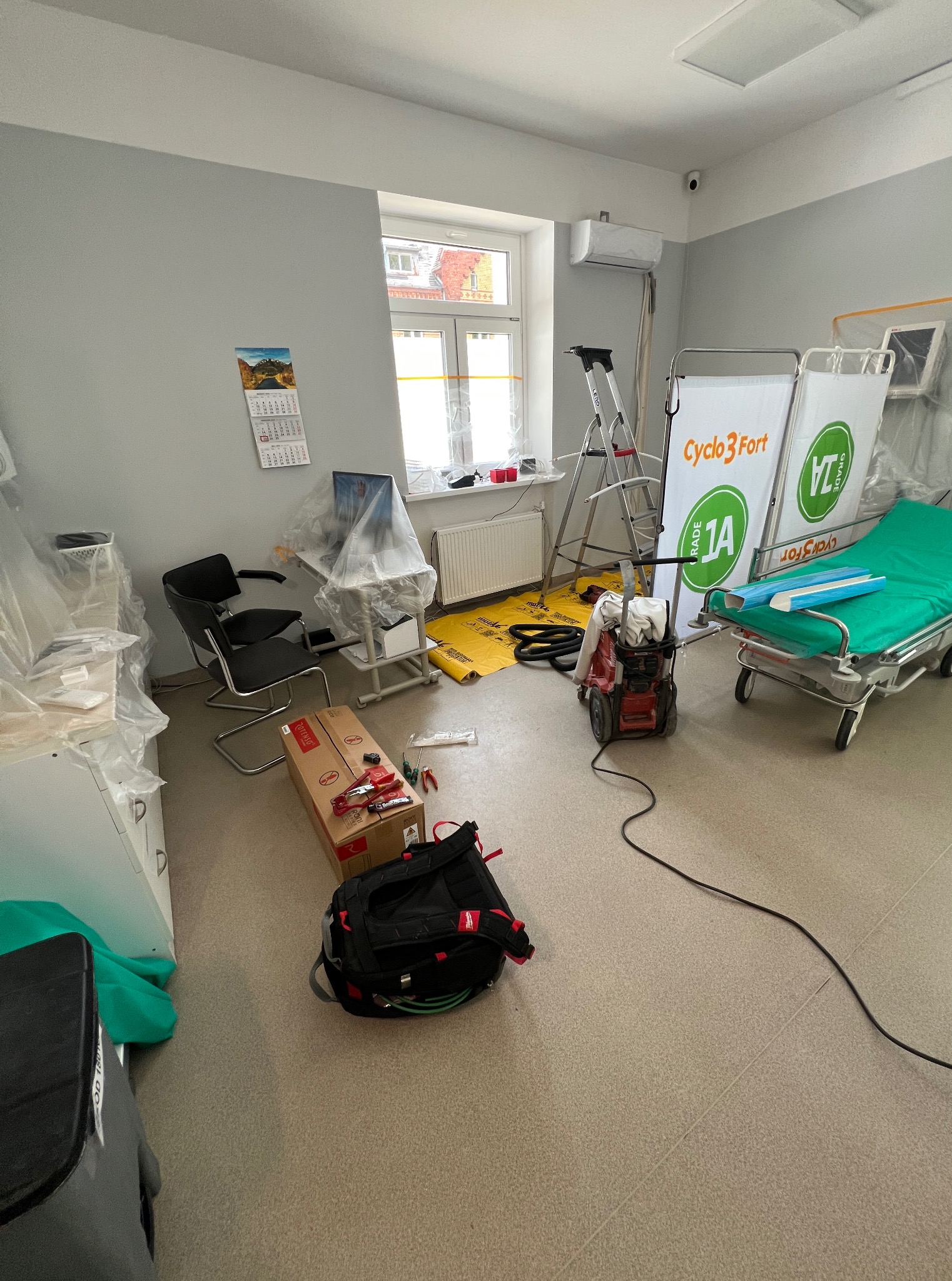 Montaż klimatyzacji w szpitalu: jednostka wewnętrzna, drabina, narzędzia, folia ochronna, łóżko szpitalne. Etap instalacji w sterylnym otoczeniu.