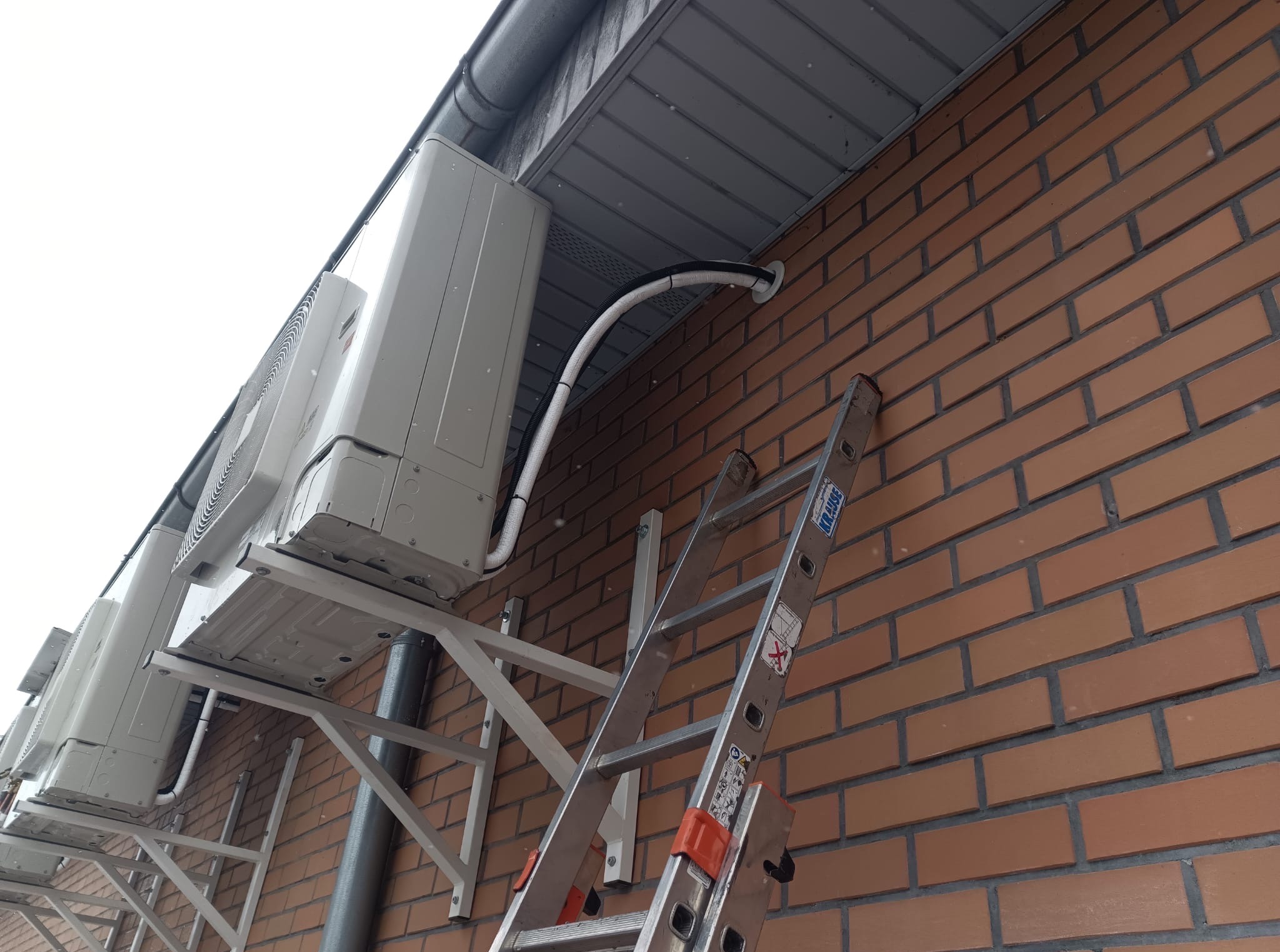 Instalacja klimatyzacji na ceglanej ścianie budynku. Widoczne jednostki zewnętrzne i drabina Krause. Ujęcie z dołu, podkreślające montaż.