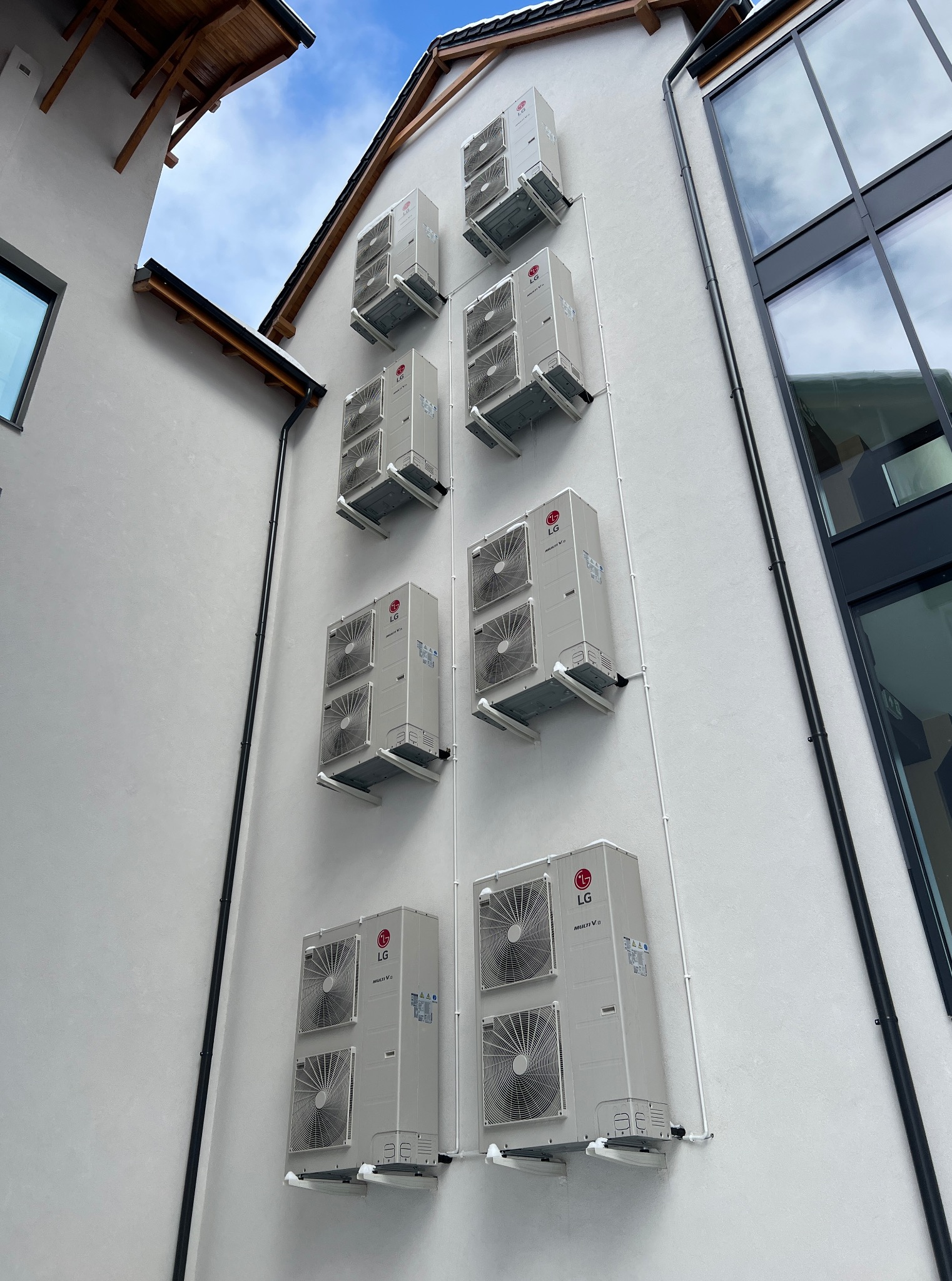 Fasada budynku z zamontowanymi jednostkami zewnętrznymi klimatyzacji LG Multi V, widoczne białe rurki instalacyjne. Ujęcie z dołu, budynek z nowoczesną architekturą.