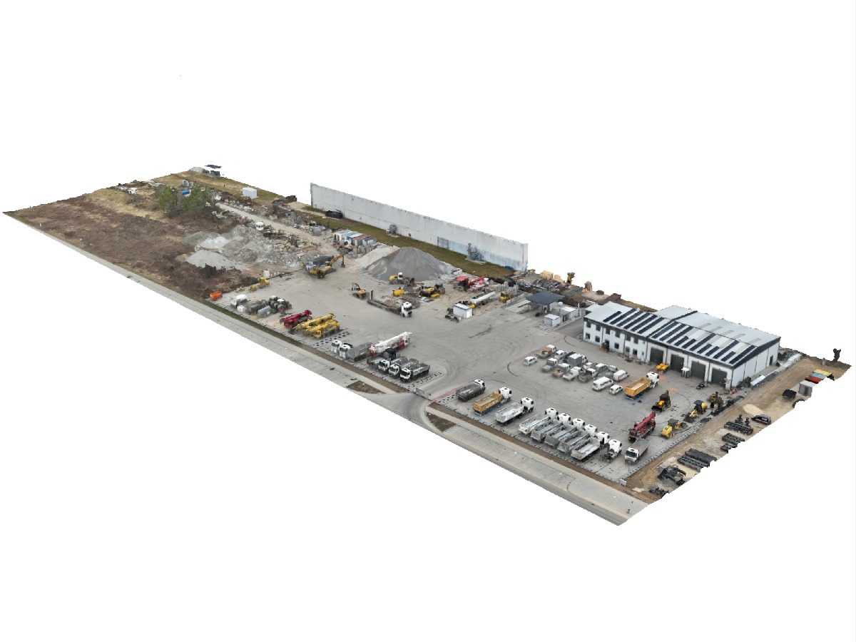 Szeroki widok z lotu ptaka na plac budowy z budynkiem magazynowym, ciężarówkami, maszynami budowlanymi i składowanym materiałem. Widoczne panele słoneczne na dachu budynku.