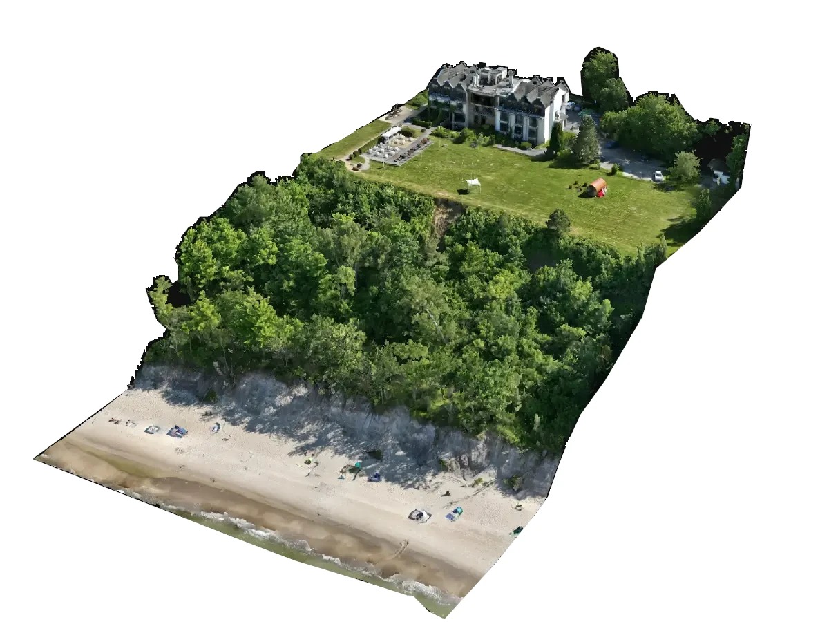 Widok z lotu ptaka na budynek hotelowy z zielonym trawnikiem, otoczony drzewami i plażą z piaskiem. Wyraźne, naturalne kolory i oświetlenie.