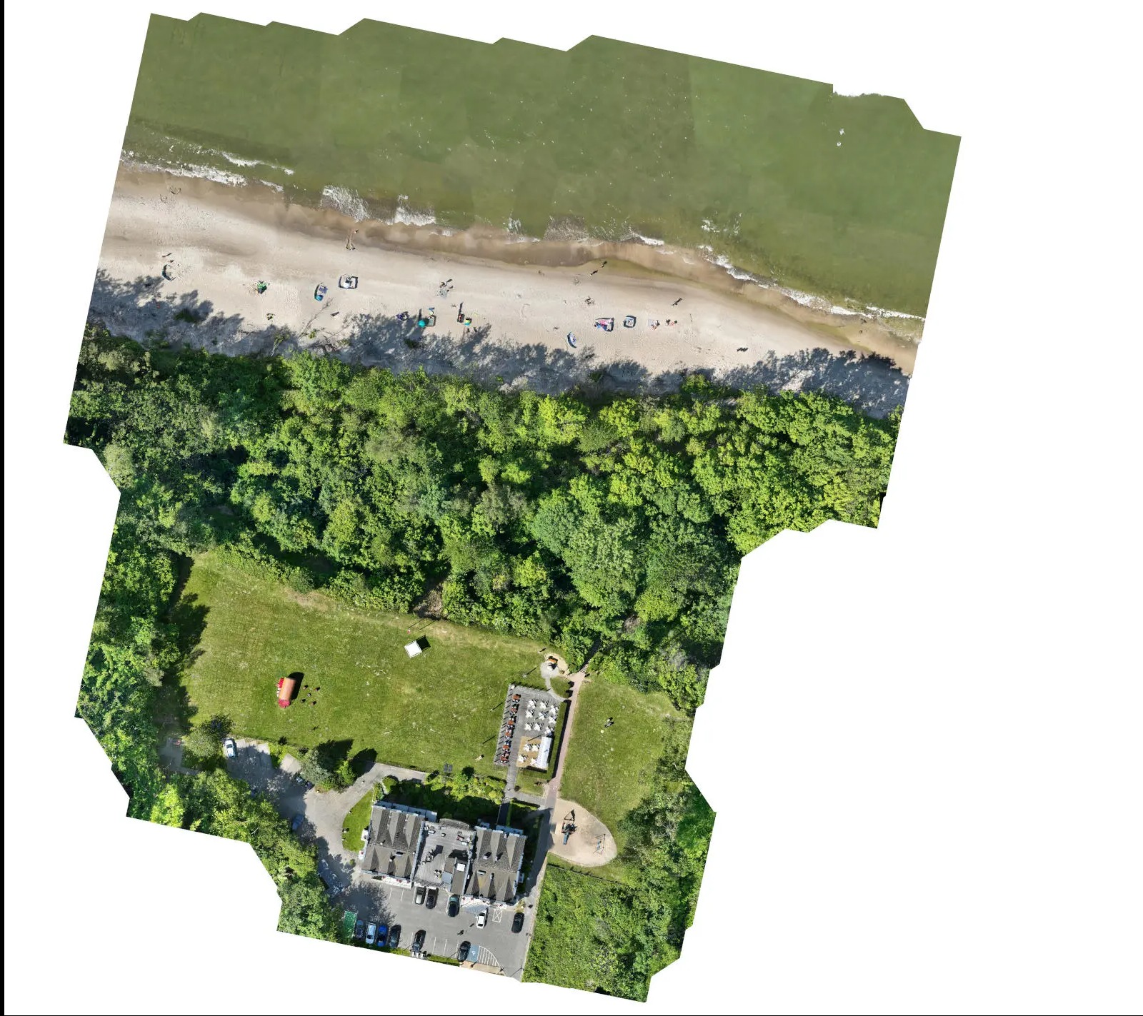 Nietypowy widok z drona na budynek z parkingiem, przylegający do plaży z turystami i lasu. Ujęcie z góry, zniekształcone krawędzie kadru.