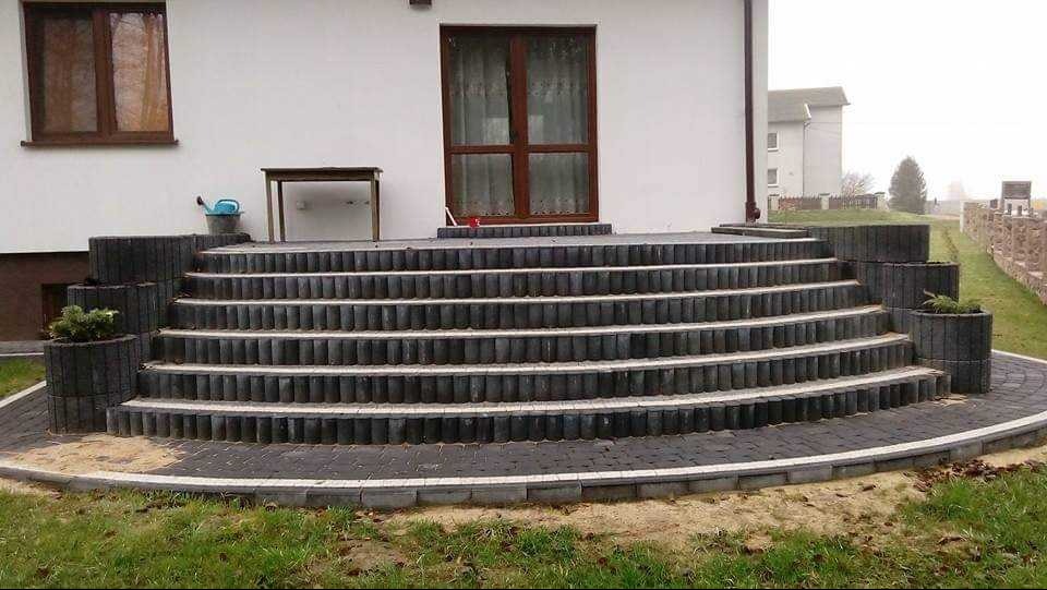 Schody wejściowe z kostki brukowej w Lubawie, prowadzące do domu. Widoczne donice z roślinami i elementy wykończeniowe, tworzące estetyczne przejście.