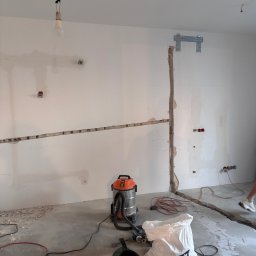 Patryk Budziszewski - Przygotowanie pod instalację klimatyzacji: bruzdy w ścianie, wspornik montażowy, odkurzacz przemysłowy i worek gruzu na szarym, betonowym podłożu.