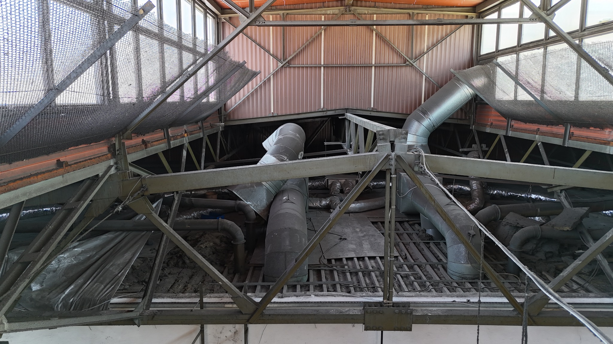 Metalowa konstrukcja dachu z systemem wentylacji, widok od dołu, oświetlenie dzienne. Elementy instalacji w szarym odcieniu.