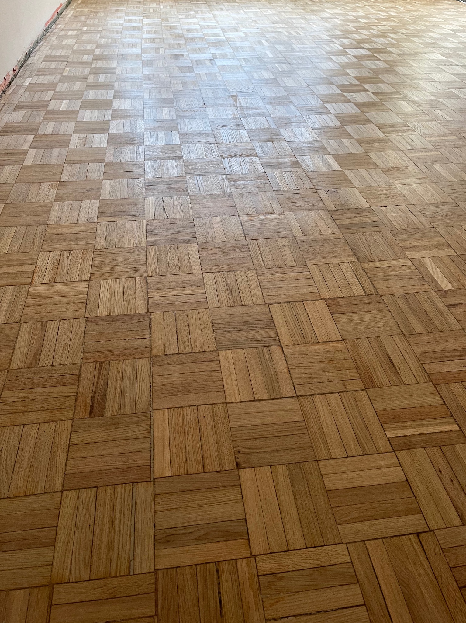 Parkiet ułożony w kwadraty z jasnego drewna, widok z góry, z delikatnym połyskiem. Układanka parkietowa z wyraźnym usłojeniem, wypełniająca całą przestrzeń kadru.