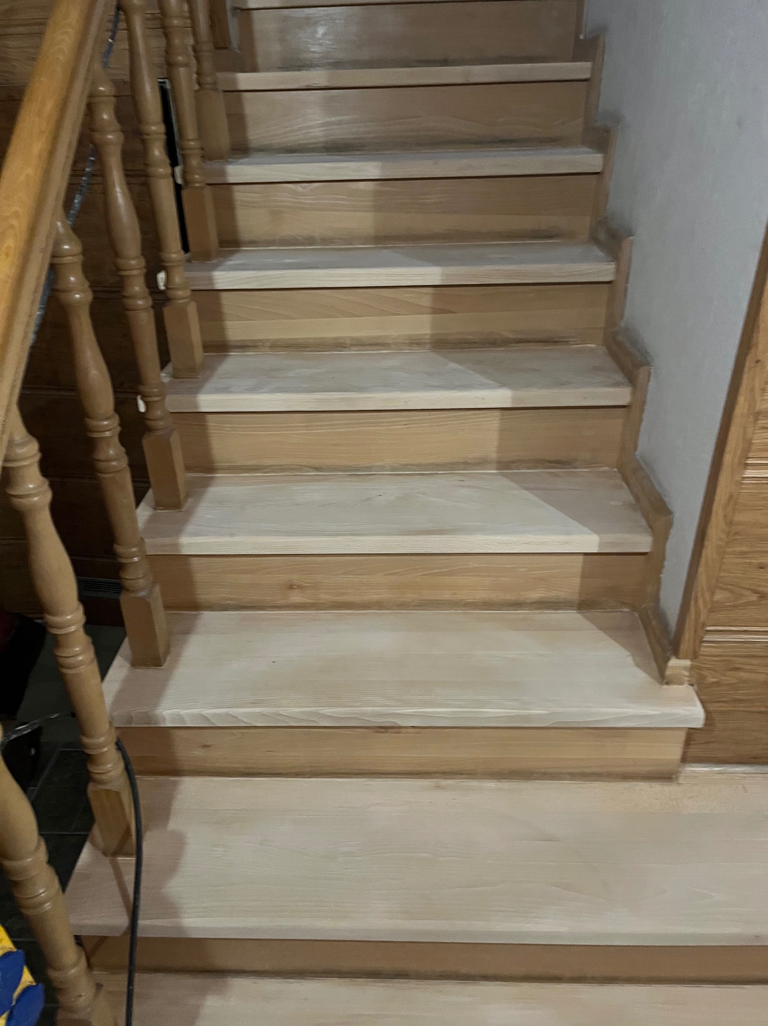 Jasne, drewniane schody z balustradą po renowacji, widok z dołu. Naturalne oświetlenie podkreśla strukturę drewna. Detal wykończenia stopni.